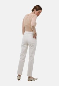 Haut beige à manches longues associé à un pantalon blanc taille haute. Le pantalon a une coupe slim et des poches arrière, complété par des chaussures beiges.