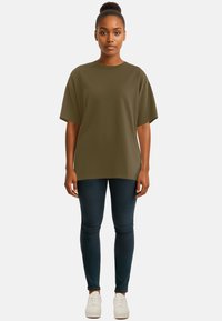 T-shirt oversize verde oliva con maniche corte, abbinato a jeans scuri e sneakers bianche, caratterizzato da una texture di tessuto liscia.