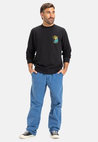 Black sweatshirt with a graphic design, featuring a turquoise detail. Worn with light blue pants and black sneakers.