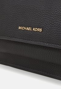 Zwarte leren handtas met een gestructureerd oppervlak. Gouden "MICHAEL KORS" logo prominent weergegeven. Strakke lijnen en subtiele stiksels accentueren het ontwerp.