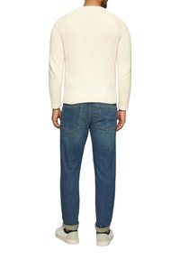 Cremfarbener Strickpullover mit ribbeltem Saum, kombiniert mit hellblauen Jeans und weißen Turnschuhen. Der Pullover hat eine strukturierte Gestaltung.