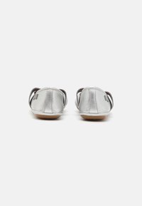 Ballerine metalliche argento con punta arrotondata, materiale in pelle morbida, cinturini elasticizzati alla caviglia e suola in gomma flessibile.