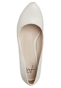 Beżowe płaskie buty z wydłużonym noskiem, wykonane z gładkiego syntetycznego materiału, o minimalistycznym designie, z otwartymi bokami i płaską podeszwą. Wnętrze ma subtelną wyściółkę.