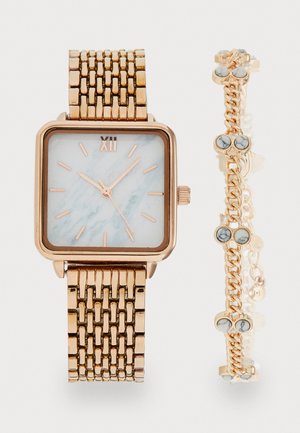 Rožu zelta taisnstūra pulkstenis ar marmora rakstu seju un zelta saites aproci. Papildus ar ķēdes aproci, kas rotāta ar dekoratīvām zilām akmeņiem.