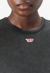 T-shirt en coton gris foncé avec un col arrondi et un petit logo brodé blanc et rouge sur la poitrine. Texture lisse.