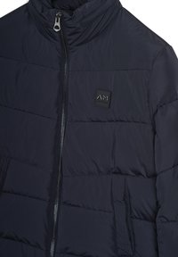 Tamno plavi kvadratni jakna s patentnim zatvaračem, visokim ovratnikom, dva bočna džepa i malim kvadratnim brendiranim logotipom na prsima.