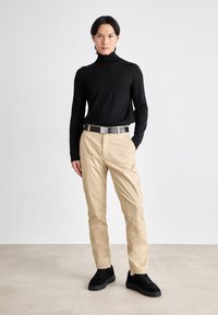 Black turtleneck sweater, beige trousers, black belt with metallic buckle, black sneakers. Smooth textures, fitted design, neutral color palette.