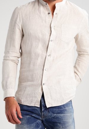 Uomo che indossa una camicia di lino beige chiaro, a maniche lunghe con bottoni e colletto alla coreana, abbinata a jeans in denim.