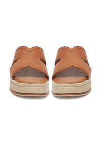 Egy pár világosbarna bőr, slip-on szandál vastag bézs talppal, nyitott orral és oldalsó kivágásokkal, elölről bemutatva fehér háttér előtt.