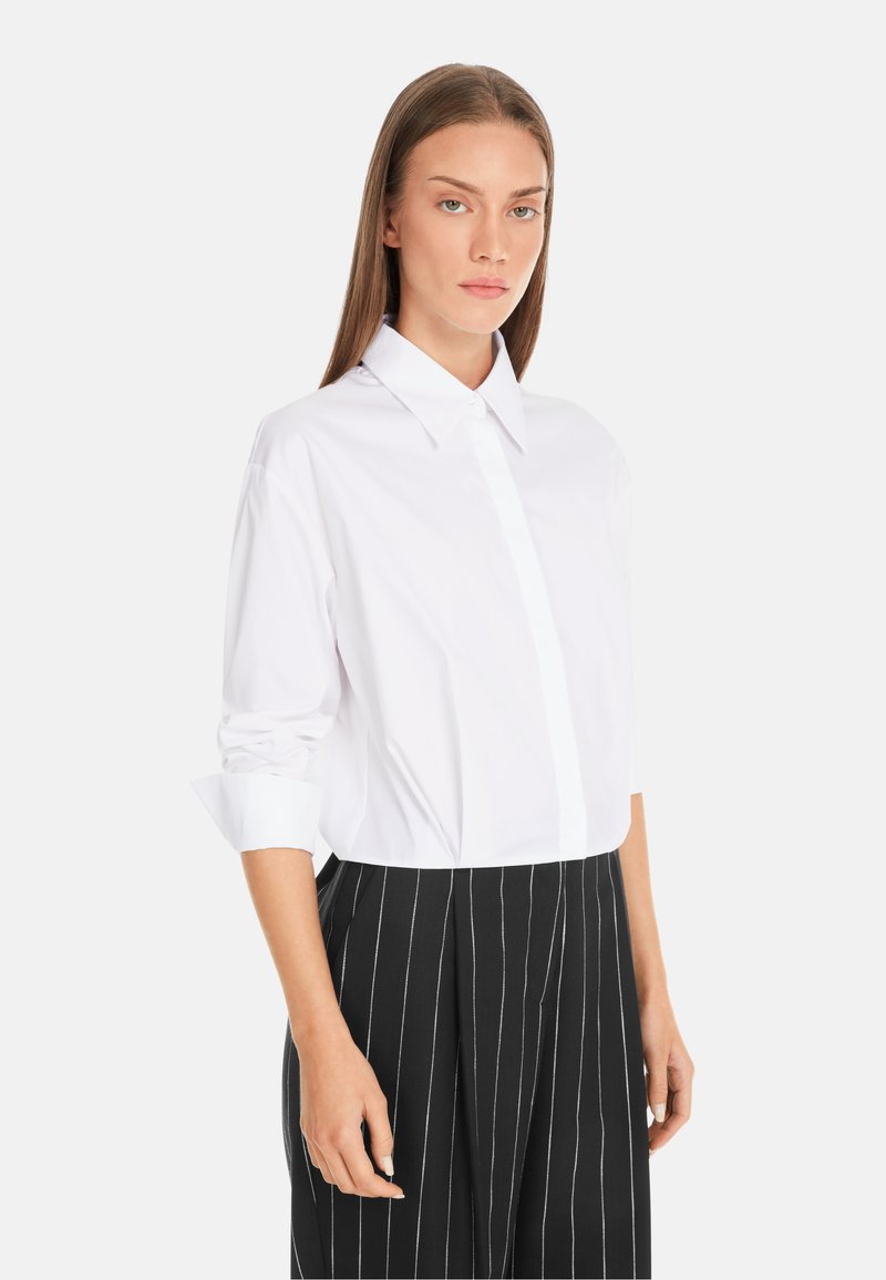 White collared button-up shirt with long sleeves, featuring a smooth texture. Paired with black pinstriped trousers.