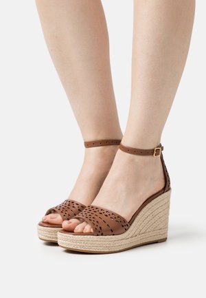 Brązowe sandały na klinie z perforowanej skóry, z platformą owiniętą juty, z paskiem na kostce i zaokrąglonym otwartym noskiem.
