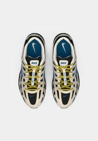 Nike skriešanas apavu pāris ar melnām, baltām un zilām akcentiem, dzeltenām šņorēm un Nike swoosh logotipiem uz zolēm un sāniem.