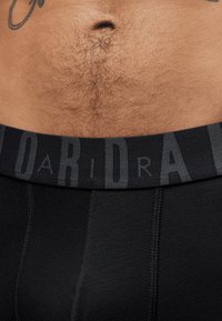 Boxers noirs avec une ceinture élastique noire portant des lettres gris clair. Le matériau semble lisse avec une ceinture légèrement texturée.