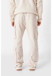 Beige Cargo-Hosen mit Seitentaschen, taillierter Schnitt am Saum, aus weichem Stoff, kombiniert mit hellen Sneakers.