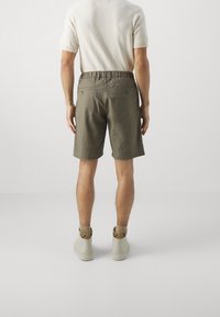 Shorts da uomo color khaki con cintura elasticizzata, due tasche posteriori e vestibilità comoda, abbinati a sneaker alte color beige chiaro.