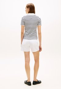 Μπλε ναυτικό και λευκό ριγέ πόλο πουκάμισο με γιακά, σε συνδυασμό με λευκό σορτς. Το μοντέλο φοράει μαύρα λουστρινά παπούτσια, φανερό από πίσω. Ομαλή υφή.