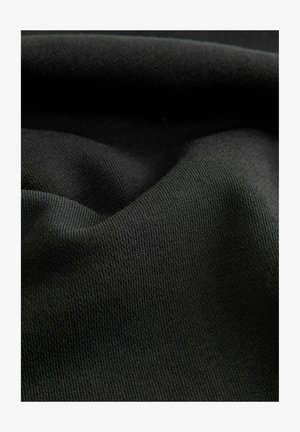 Black fabric with a textured knit pattern, featuring a smooth surface and folds that highlight its drape and flexibility.