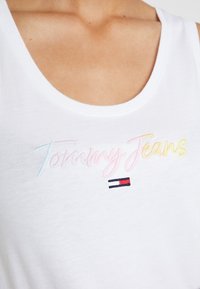 Bílý tílko s výšivkou "Tommy Jeans" v pastelových barvách a červenobílo-modrou akcentní logem pod ním.