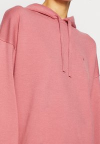 Felpa con cappuccio rosa chiaro in materiale a maglia testurizzata, caratterizzata da una vestibilità rilassata e un cordoncino al collo. Dettaglio logo discreto sul petto.