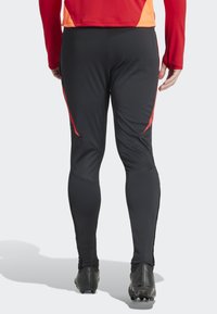 Zwarte sportleggings met rode zijkanten, voorzien van een strak ontwerp en een gladde textuur, geschikt voor sport of actieve kleding.