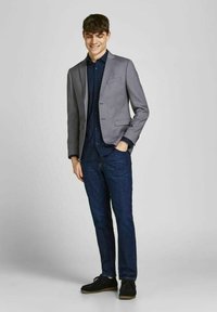 Grå blazer over en marineblå skjorte med prikker, parret med mørke jeans og sorte sko. Slim fit design med frontlommer og en glat tekstur.