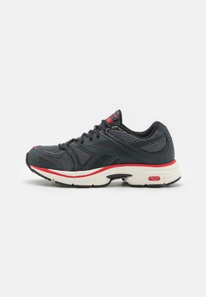 Black athletic shoe with mesh upper, red accents, and cushioned white sole. Features textured design and lace-up closure for secure fit.