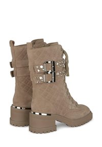 Stivaletti in camoscio beige chiaro con lacci, texture trapuntata, borchie argento e dettagli con doppia fibbia. Presentano un tacco robusto e una suola in gomma.