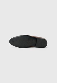 Black rubber sole with textured surface, attached to a sleek brown leather upper, featuring a minimalist design and subtle branding detail.