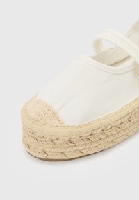 Hvid lærred espadrille med rund tå, flettet jute-sål og kontrastfarvet beige gummitrim langs kanten. Indeholder en stropdetalje.