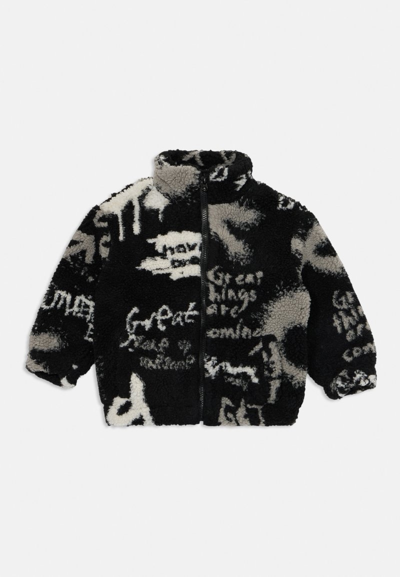 Chaqueta de forro polar negra y crema con un alto cuello, cierre con cremallera en la parte delantera y patrones de texto abstractos. Textura suave y corte oversize.