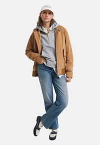 Pruun sametjakker halli kapuutsiga, sinised teksad ja mustad-valged jalanõud. Valge müts, millel on tekst ja lõdvestunud sobivus.