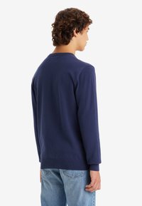 Marineblauwe longsleeve shirt van zachte stof, met een ronde hals en geribde manchetten. Draag het met lichtblauwe spijkerbroeken voor een relaxte pasvorm.