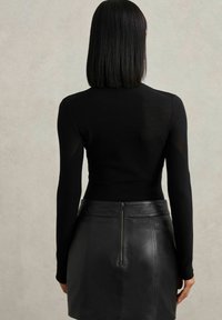 Schwarzer, taillierter Pullover mit langen Ärmeln, kombiniert mit einem schwarzen Leder-Minirock, der einen zentralen Reißverschluss auf der Rückseite hat.