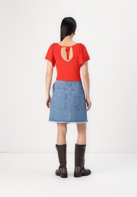 Rød ribbete topp med pufferm, lav rygg med bånddetalj. Lys blå denimskjørt med to baklommer og slitt kant. Brune knehøye støvler.