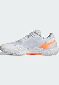 Valkoinen urheilukenkä, jossa on teksturoitu verkkomateriaali yläosassa, oranssit yksityiskohdat ja segmentoitunut kumipohja, varustettuna nauhoilla ja pehmustetulla nilkkaremmillä.