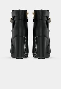 Μαύρες δερμάτινες μπότες μέχρι τον αστράγαλο με χοντρό τακούνι, χαρακτηριστικά μιας φαρδιάς λωρίδας και χρυσής αγκράφας. Λείο υλικό και κομψός σχεδιασμός.