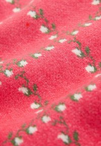Szövet, amely rózsaszín háttérrel, fehér virágokból és zöld levelekből álló virágmintával, puha textúrával és enyhén bolyhos felülettel rendelkezik.