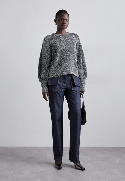 Grå tekstureret sweater med ballonærmer, parret med mørkeblå lige ben jeans med lommefritter og sorte hæle.