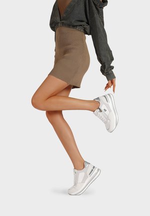 Sneakers bianchi con accenti argentati, pannelli in rete e suola testurizzata. Indossati con una gonna marrone aderente, che mostra un profilo laterale del calzature.