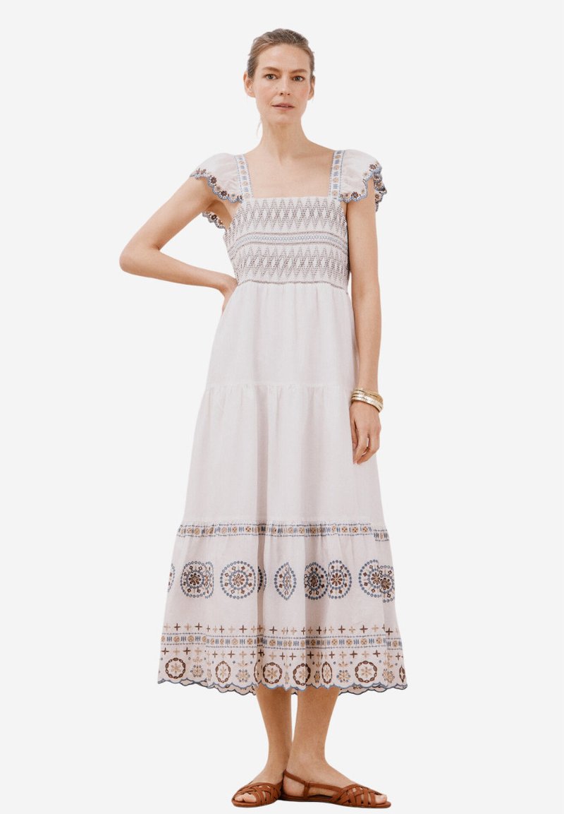 Robe maxi en coton blanc avec des détails brodés, décolleté carré et manches courtes à volants. Caractéristiques d'un ourlet en étages avec des motifs décoratifs.
