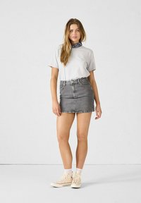 Falda de mezclilla gris combinada con una camiseta gris clara. El atuendo incluye unas zapatillas altas beige y una bufanda de pañuelo azul marino.