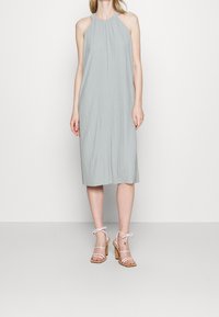 Vestido de tirantes en gris claro con un tejido texturizado, de longitud hasta la rodilla, combinado con sandalias de tacón alto con tiras transparentes y tacón de corcho.