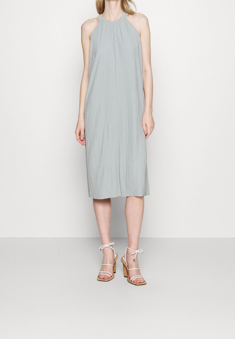 Vestido de tirantes en gris claro con un tejido texturizado, de longitud hasta la rodilla, combinado con sandalias de tacón alto con tiras transparentes y tacón de corcho.