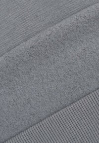 Szary materiał o gładkim splotem i miękkiej, puszystej teksturze. Zawiera prążkowany mankiet na dole, co tworzy kontrast w fakturze.