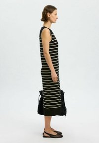 Robe maxi sans manches à rayures noires et blanches, coupe slim, avec une partie inférieure entièrement noire. Les accessoires incluent un sac fourre-tout tissé noir et des chaussures plates.