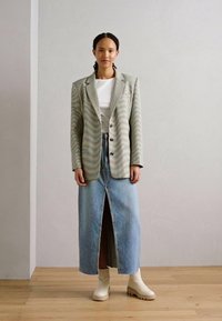 Blazer oversize rayé en gris clair et vert, porté sur un t-shirt blanc, associé à une longue jupe en denim et des bottines crème.