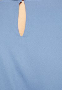 Modrý textil s hladkou strukturou a detailem ve tvaru klíčové dírky. Barva je jemná a jednotná, což zvýrazňuje plynulost látky.