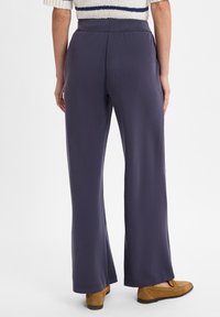 Marineblauwe wijde broek met een gladde textuur en een hoge taille, gecombineerd met suède bruine loafers, gezien vanaf de achterkant.