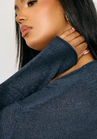 Mörkblå texturerad stickad topp med långa ärmar, som har en avslappnad passform och en subtil lyster, som framhäver mjuka sömnadsdetaljer.