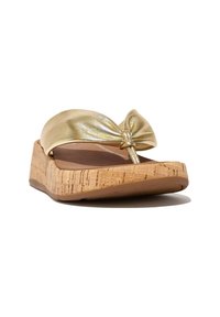 Gouden metallic slide sandaal met een strikaccent, kurken wigzool en een glad voetbed. Het ontwerp heeft een afgeronde vorm en een getextureerde zool.